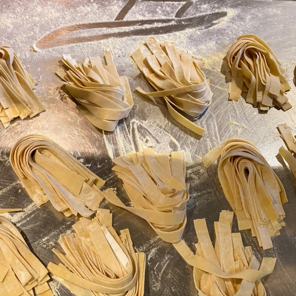 Fresh handmade pappardelle nests on a floured kitchen bench
